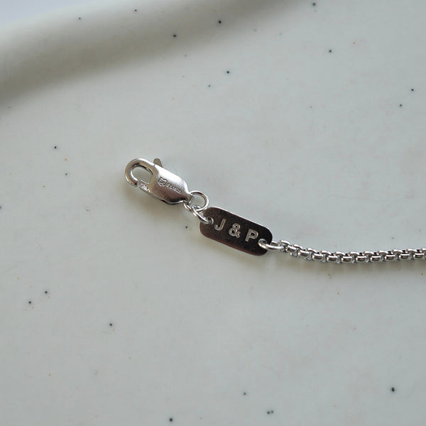 Detailaufnahme einer silbernen Halskette mit Gravur von Initialen auf kleinem Anhänger zeigt präzise Umsetzung personalisierter Schmuckgravur mit feiner Verarbeitung Sprezzi Fashion