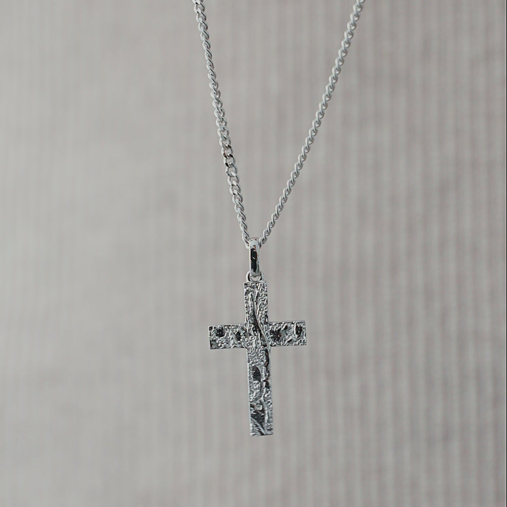 Nahaufnahme einer Herren Halskette aus 925 Sterling Silber mit Kreuz Anhänger, dessen gehämmerte Oberfläche das Licht unregelmäßig reflektiert und die markante, strukturierte Form deutlich hervorhebt Sprezzi Fashion