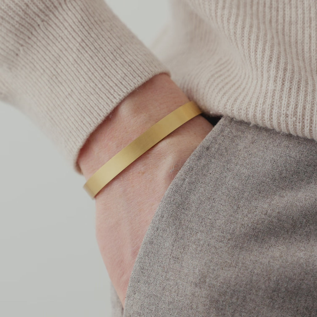 Der matte goldene Armreif aus Edelstahl ergänzt das Outfit stilvoll, während die klare Form und die warme Farbnuance einen hochwertigen Eindruck vermitteln Sprezzi Fashion